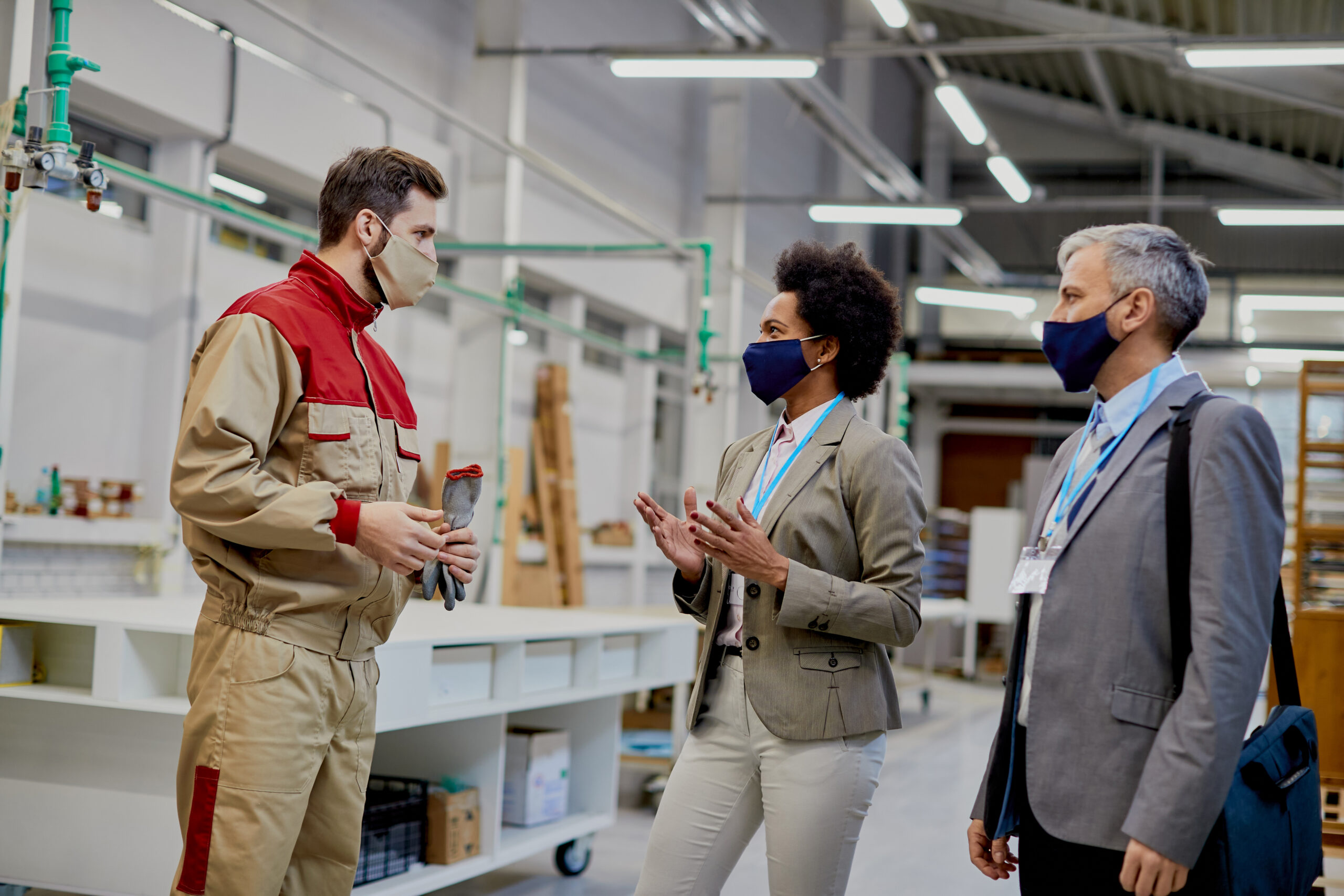 Business people communicating with male worker while visiting woodworking factory during coronavirus pandemic.